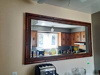 Image of large rectangular mirror with dark wood bamboo-style frame hanging on wall, reflecting kitchen interior.