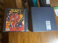 Two blue binders containing basketball trading cards. One binder has a Beckett magazine on top while the other is closed.