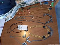 Wide view of various costume necklaces arranged on fabric and wooden surface showing variety of materials and designs including chains, beads, and pendants.
