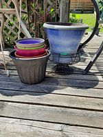 Blue metal planter on black stand with nested plastic planters in a dark brown plastic planter on wooden deck, outdoor setting.