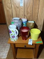 Seven ceramic and glass items including planters, vases and jug arranged on a wooden table with brown wood panel wall background.