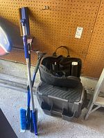 Side view of the roadside emergency kit, Craftsman organizer on top, and two snow brushes leaning against a wall.