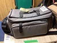 Gray fabric carrying bag with multiple compartments and adjustable straps placed on top of wooden surface.