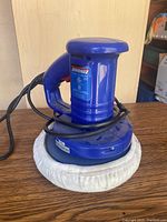 Front view of one blue Simoniz 8" random orbit polisher/waxer with power cord wrapped around it on a wooden surface.