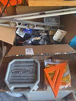 Box containing metal spirit levels, orange carpenter square, safety goggles, assorted drill bits in plastic case, assorted small items.
