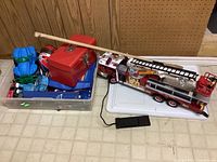 Photo showing clear container holding multiple small toys including planes, dinosaur figures, and toy vehicles, with a red metal box on top and a wooden hurling stick.