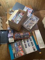 Wide view of table showing cardboard box of cards, plastic tub, binders, storage boxes and small bat