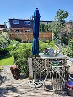 Full view of closed blue outdoor patio umbrella standing on wooden deck with garden background.