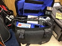 Overview photo of camera bag open showing Pentax MX camera, Sunpak flash, Kodak film, and camera strap.