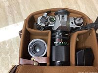 Top-down view of camera body in padded insert with two lenses, flash and accessory box
