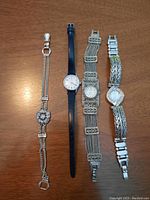 Four watches laid side by side on wood surface showing variety of bracelet bands and watch faces.