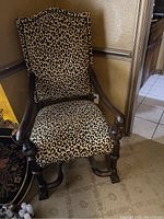 Full side angle of the leopard print armchair showing the wooden armrests and carved legs