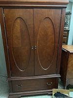 Front view of wooden armoire with double doors and bottom drawer