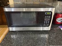 Front view of Emerson microwave oven placed on kitchen counter, showing stainless steel exterior and control panel screen displaying time.