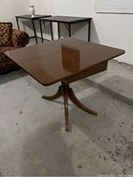 Full view of the wooden flip top table showing the pedestal base and four legs with brass caps.