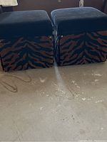 Photo of two custom animal print rolling ottomans, square shape, with dark fabric tops and tiger pattern sides.