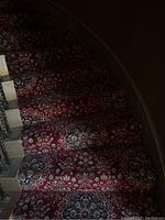 Close-up of carpeted stairs showing the detailed floral and medallion red and blue pattern on each step.