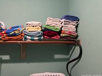 Photo showing multiple stacks of assorted colorful towels on a wooden shelf against a light green wall.