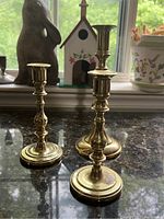Set of three brass candlesticks displayed on a reflective surface near a window, shows the overall size and design.