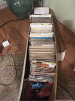 Long cardboard box filled with assorted comic books stored upright, showing protective sleeves.