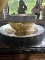 Perspective view showing the gold and silver decorative bowl placed on the matching plate with visible textured and worn surfaces.