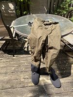Full view of brown hip waders with black attached boots on outdoor patio table.
