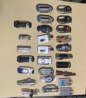 Photo of 18 assorted butane lighters arranged on a beige surface showing various styles and colors.