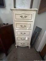 Full view of tall white French provincial lingerie chest with five drawers and decorative metal handles