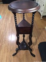 Front view of the vintage mahogany side table showing round top, twisted legs, triangular middle shelf with drawer, and tripod base
