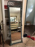 Full-length mirror in green metal frame with decorative scroll and ornamental corners.