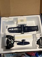 Black and blue F4U Corsair airplane model and remote controller inside white foam packaging insert.
