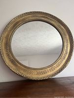 Front view of round ornate gold framed mirror on wooden surface against white wall