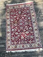 Full view of the Oriental rug showing the red floral central field and beige floral border with fringed edges.
