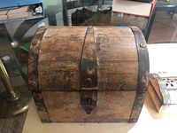 Photo of a large wooden chest-shaped trinket box with metal straps and lock showing aged and worn surface