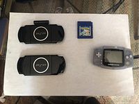 Top-down view showing two PSP back shells, one Game Boy Advance and one Pokemon Blue cartridge.