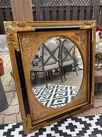 Front view of square gold and black frame with round mirror reflecting outdoor furniture