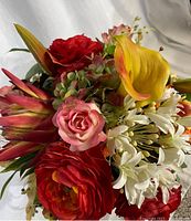 Close-up image of floral arrangement showing detailed silk flowers: red and pink roses, yellow calla lily, white agapanthus, orange lilies, and greenery.