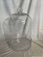 Front view of the tall clear glass dome with knobbed lid on a flat glass base.