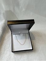 Gold chain necklace placed on a white cushioned area inside an open black jewelry box with golden edge.