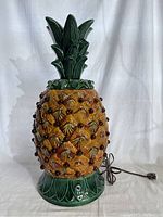 Front view of Mid-Century Modern ceramic pineapple lamp showing textured yellow and brown ceramic body with dark brown applied marble accents, green stylized leaf base and top.