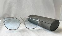 Front view of Gentle Monster Wind Wind 032 sunglasses with blue lenses and silver metal frame placed next to a black sunglasses case.