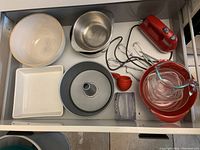 Overhead view of drawer showing all included bakeware, measuring cups, and KitchenAid hand mixer with cords and attachments.
