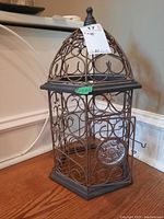 Front view of hexagonal metal cage with ornate scroll design, door, and finial top.
