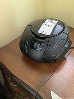 Black Sylvania SRCD261 CD player on wooden surface showing front and top-loading lid closed with display visible