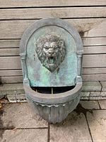 Front view of resin hanging fountain with lion head relief showing patina and basin.