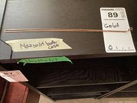 Full view of the gold chain laid flat on a dark wooden surface next to a label showing item number and measurements.