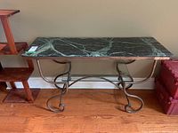Front view of the granite top hallway table with dark green granite and metal legs on wooden floor