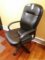 Side view of black office chair showing padded armrest, cushioned seat and back, on a wheeled five-star base set on wood floor.