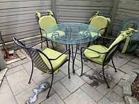 Photo showing the full patio set with round glass table and four green cushioned metal chairs.