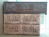Stacked view of two ceramic planters featuring classical bas-relief figure designs and one metal planter with floral embossed rose motifs on top.